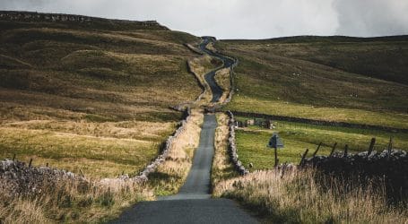 road between green grasses under cloudy sky during daytime