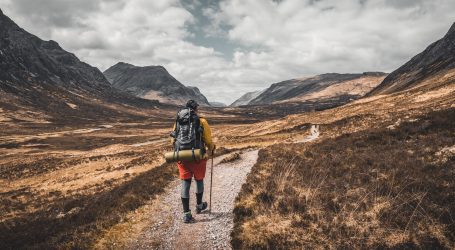 person wearing backpack walking on dirt road