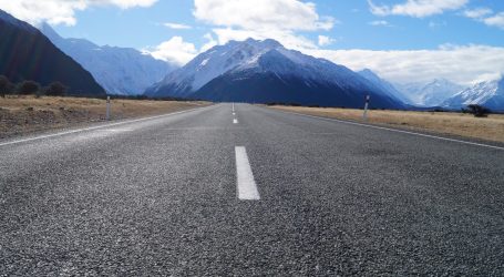 gray asphalt road near mountain range under blue sky during daytime