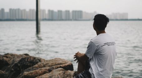 man in white shirt sitting on brown rock near body of water during daytime