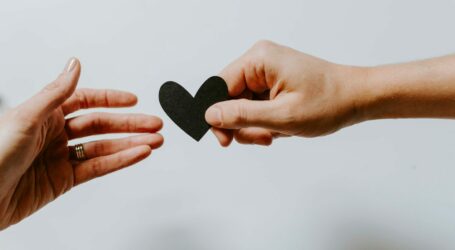 person reaching black heart cutout paper